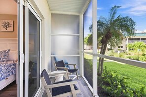Ein Balkon mit zwei Stühlen, ein Bett mit gemusterten Betttextilien und Blick auf eine grüne Landschaft mit Palmen.