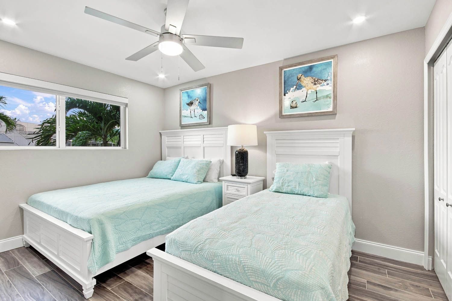 A bedroom with two beds, a ceiling fan, and artwork on the walls.