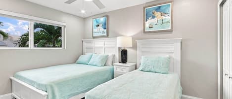 A bedroom with two beds, a ceiling fan, and artwork on the walls.