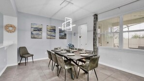 Comedor con una mesa dispuesta para seis personas, una silla gris y una lámpara colgante moderna.