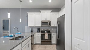 A modern kitchen with white cabinets, stainless steel appliances, and pendant lighting. - The Splash Shot - Two Bedroom Apartment, Sleeps 6 (Kissimmee)