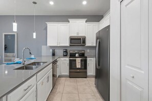 A modern kitchen with white cabinets, stainless steel appliances, and pendant lighting. - The Splash Shot - Two Bedroom Apartment, Sleeps 6 (Kissimmee)