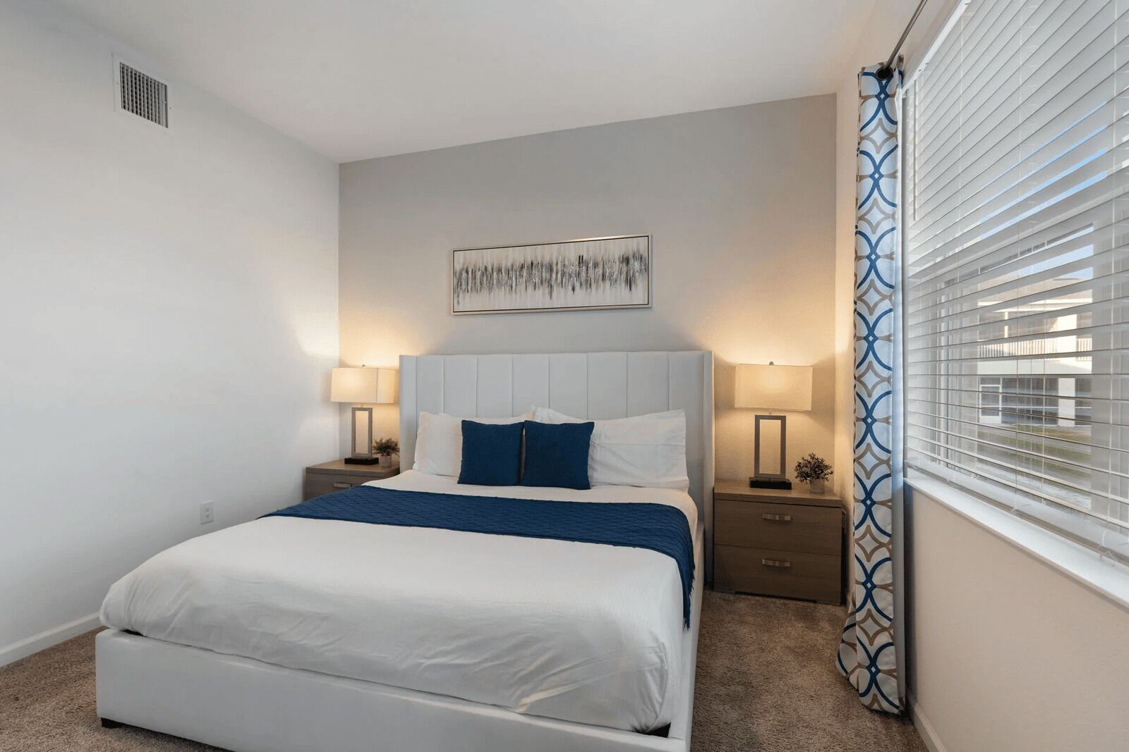 Een slaapkamer met een bed, twee nachtkastjes, een kunstwerk aan de muur en een raam met zonwering.