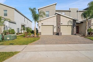 A residential building with a garage, a brick driveway, and a well-maintained lawn with palm trees. - The Splash Shot -Championsgate Resort, Amenities Included/Games Room/Free wifi (Kissimmee)