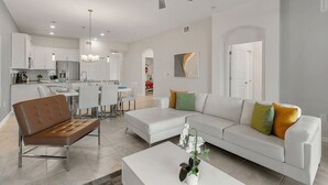 A modern living room with a sofa, coffee table, and a dining area with chairs and a table. - The Splash Shot - Two Bedroom Apartment, Sleeps 6 (Kissimmee)