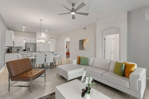 A modern living room with a sofa, coffee table, and a dining area with chairs and a table. - The Splash Shot - Two Bedroom Apartment, Sleeps 6 (Kissimmee)