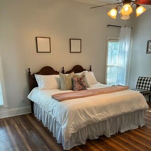 A bedroom with a large bed, wooden headboard, two framed pictures on the wall, a ceiling fan, and a window with blinds. - Southern Comfort with plenty of room for the entire family. (Byhalia)