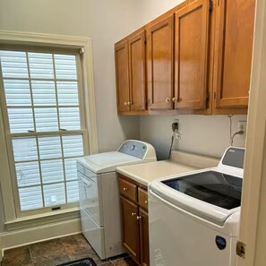 A laundry room with a washer and dryer, wooden cabinets, and a window with blinds. - Southern Comfort with plenty of room for the entire family. (Byhalia)