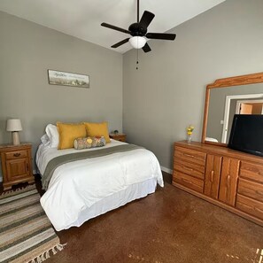 Ein Schlafzimmer mit einem Bett, einer Holzkommode, einem Deckenventilator, einem an der Wand befestigten Fernseher und einem gerahmten Bild.