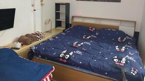 Makuuhuoneessa on kuvioitu peitto sängyllä, seinälle asennettu televisio ja sängyn yläpuolella kaupunkimaisemaa esittävä taulu.