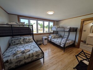 Une chambre avec deux lits superposés, un petit radiateur et une fenêtre donnant sur des maisons et des arbres.