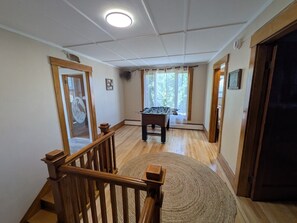 A spacious room with a wooden staircase, a foosball table, and a large window with curtains. - The Lodge at South of the Border (Canaan)