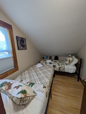 Ein kleines, gemütliches Zimmer mit zwei Betten, einem Fenster mit Jalousien, einem Wandheizgerät und einem gerahmten Bild.