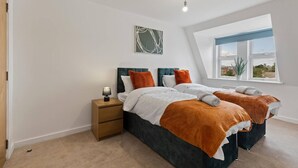 A bedroom with two beds, a nightstand, a lamp, a window with a view, and a ceiling light. - West Bridgford Luxury 2 bed 2 Bath Apartment (Nottingham)