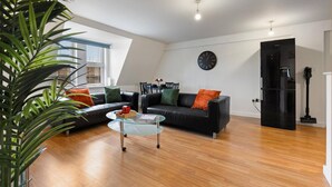 A modern living room with a glass coffee table, black leather sofa, and a clock on the wall. - West Bridgford Luxury 2 bed 2 Bath Apartment (Nottingham)
