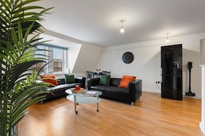Ein modernes Wohnzimmer mit einem Glastisch, einer schwarzen Ledersofa und einer Uhr an der Wand.