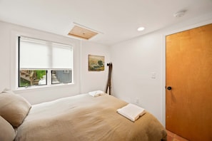 Ein Schlafzimmer mit Bett, Fenster, Tür und einem Bild an der Wand.