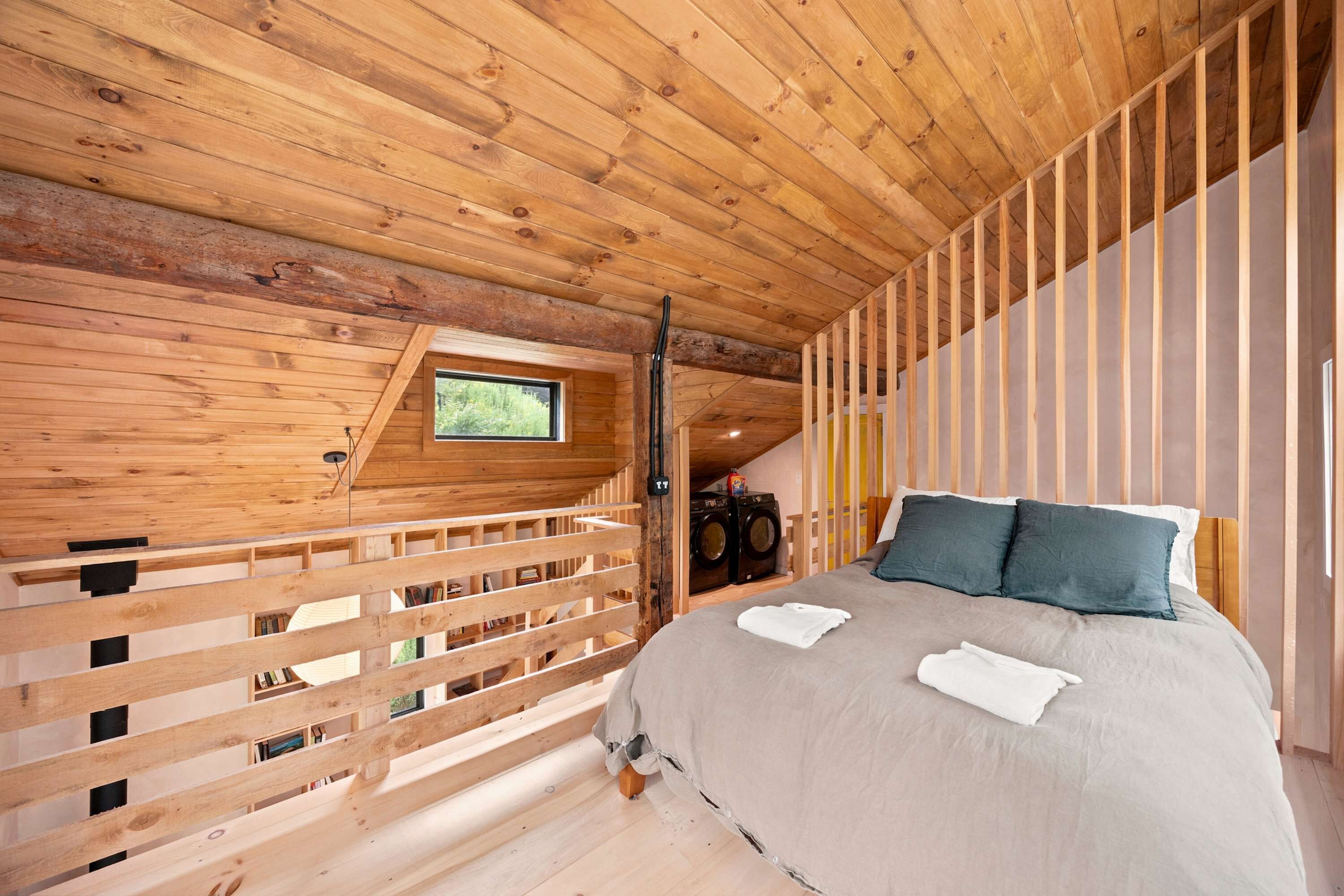A wooden cabin interior with a bed, a window, and a washing machine.