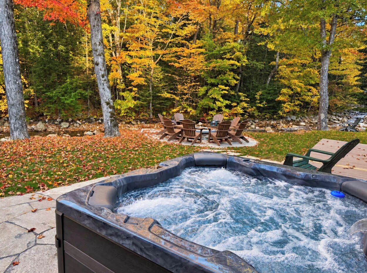 A hot tub surrounded by autumn foliage, with outdoor seating and a stone pathway.