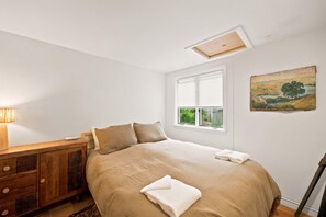 A bedroom with a bed, a wooden dresser, a window with blinds, and a painting on the wall. - The Mad River Lodge: Riverside Escape (Waterville Valley)