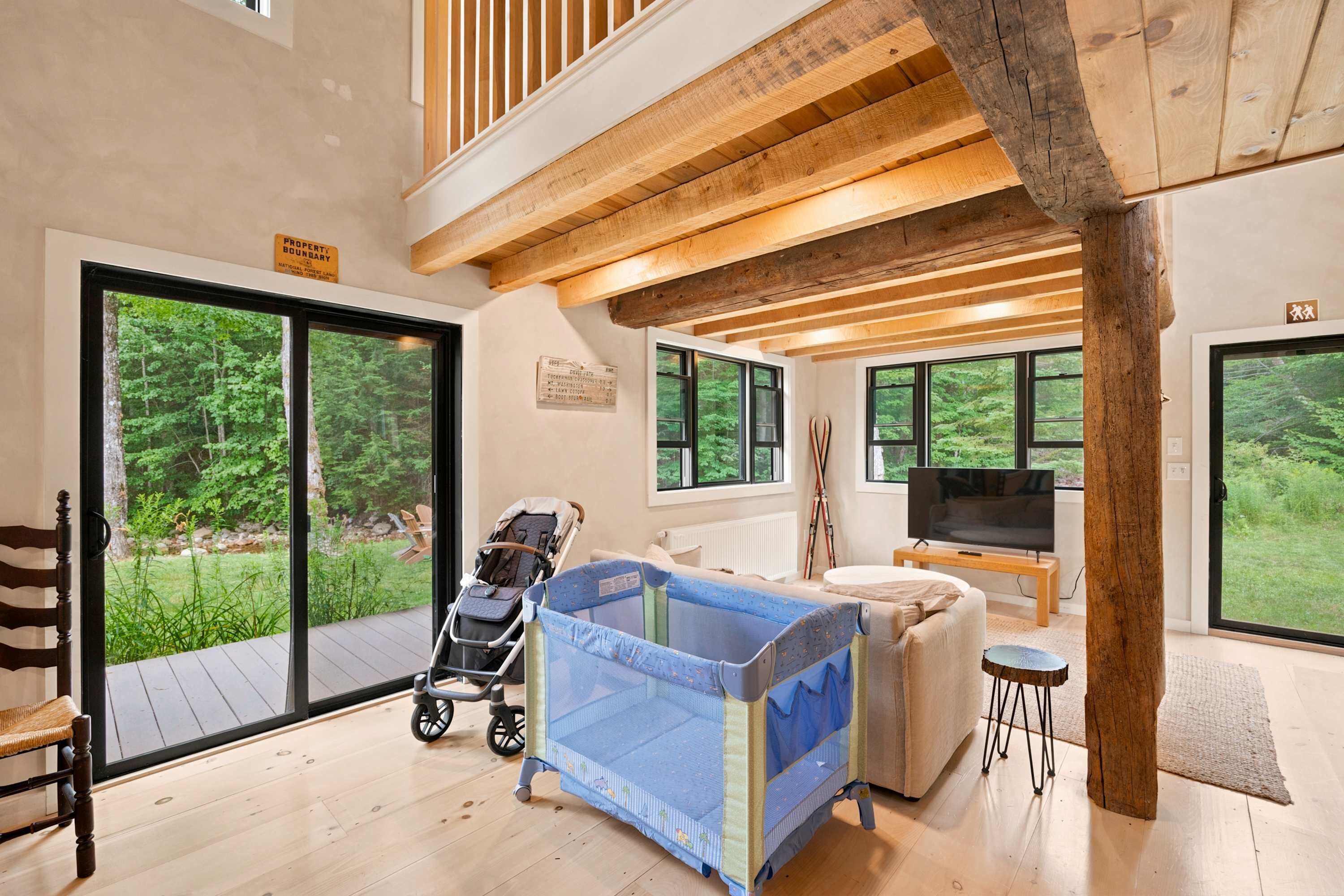 A spacious room with a large sliding glass door leading to a deck, a baby playpen, a television, and a cozy seating area.