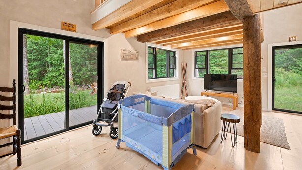 Ruime kamer met een grote schuifpui naar een terras, een babyrekkentje, een televisie en een gezellige zithoek.