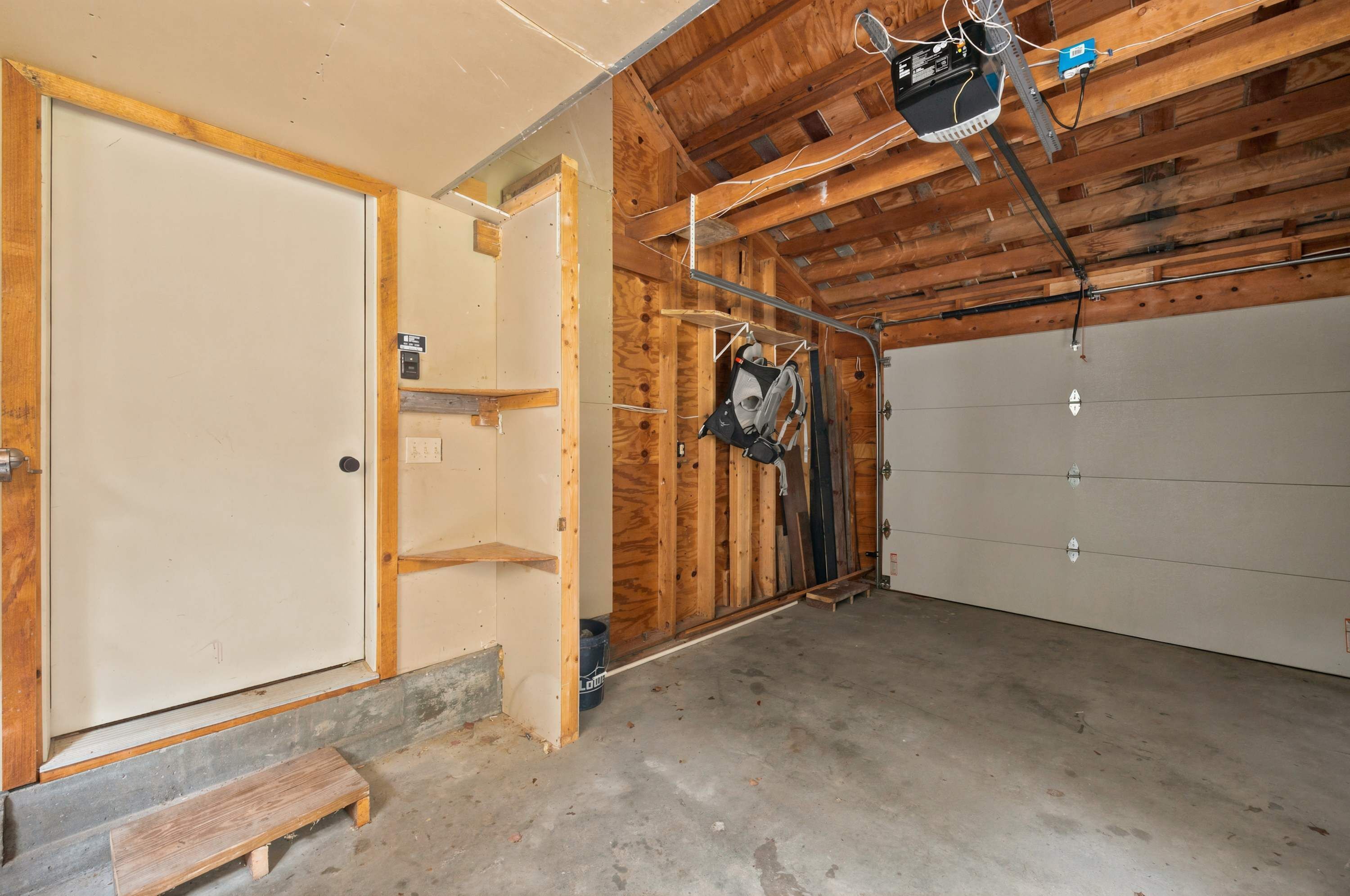 A garage with a wooden ceiling, a white door, and a concrete floor.