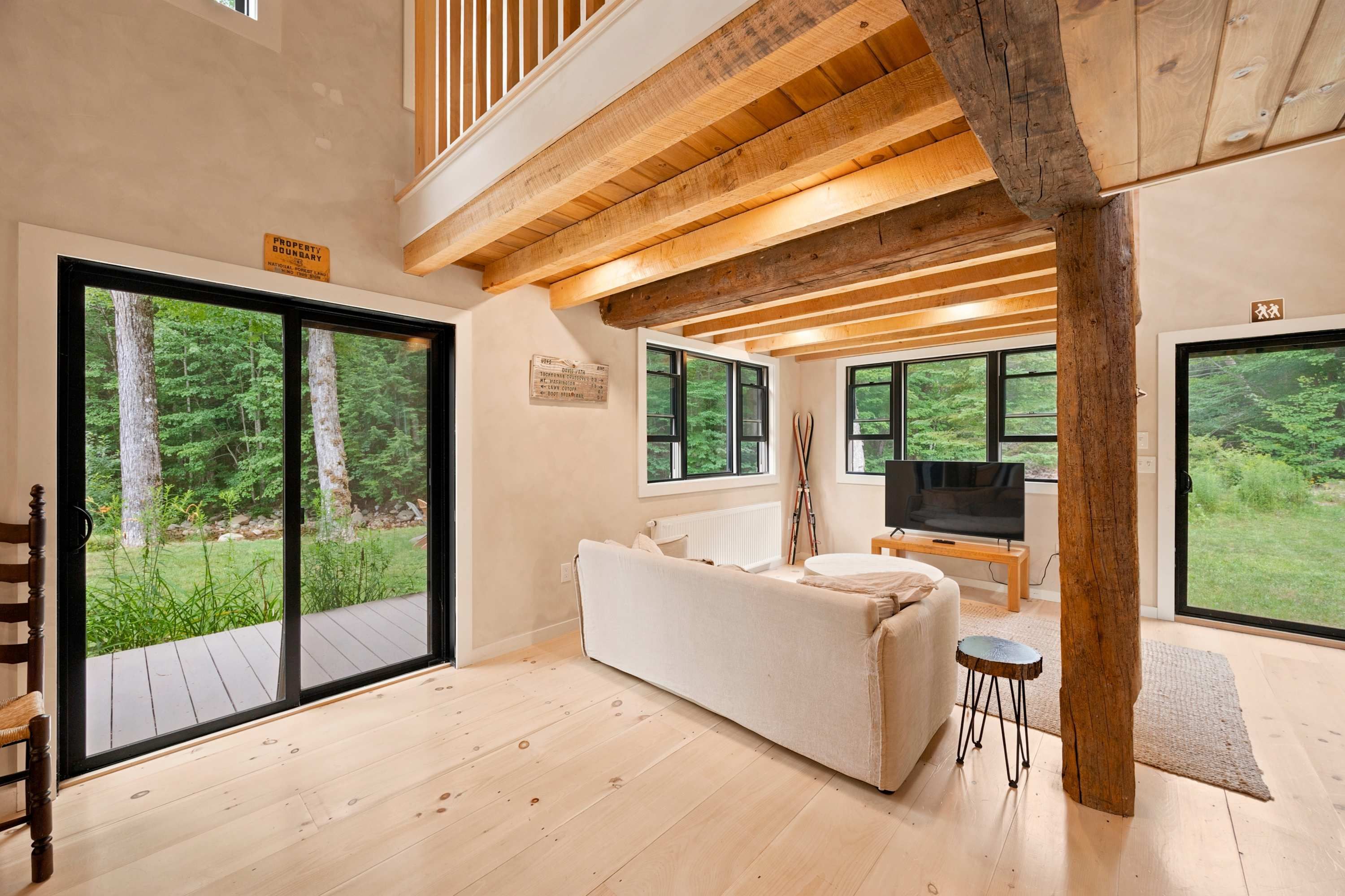 A spacious living area with a large sofa, a television, and a view of a forest through large windows.