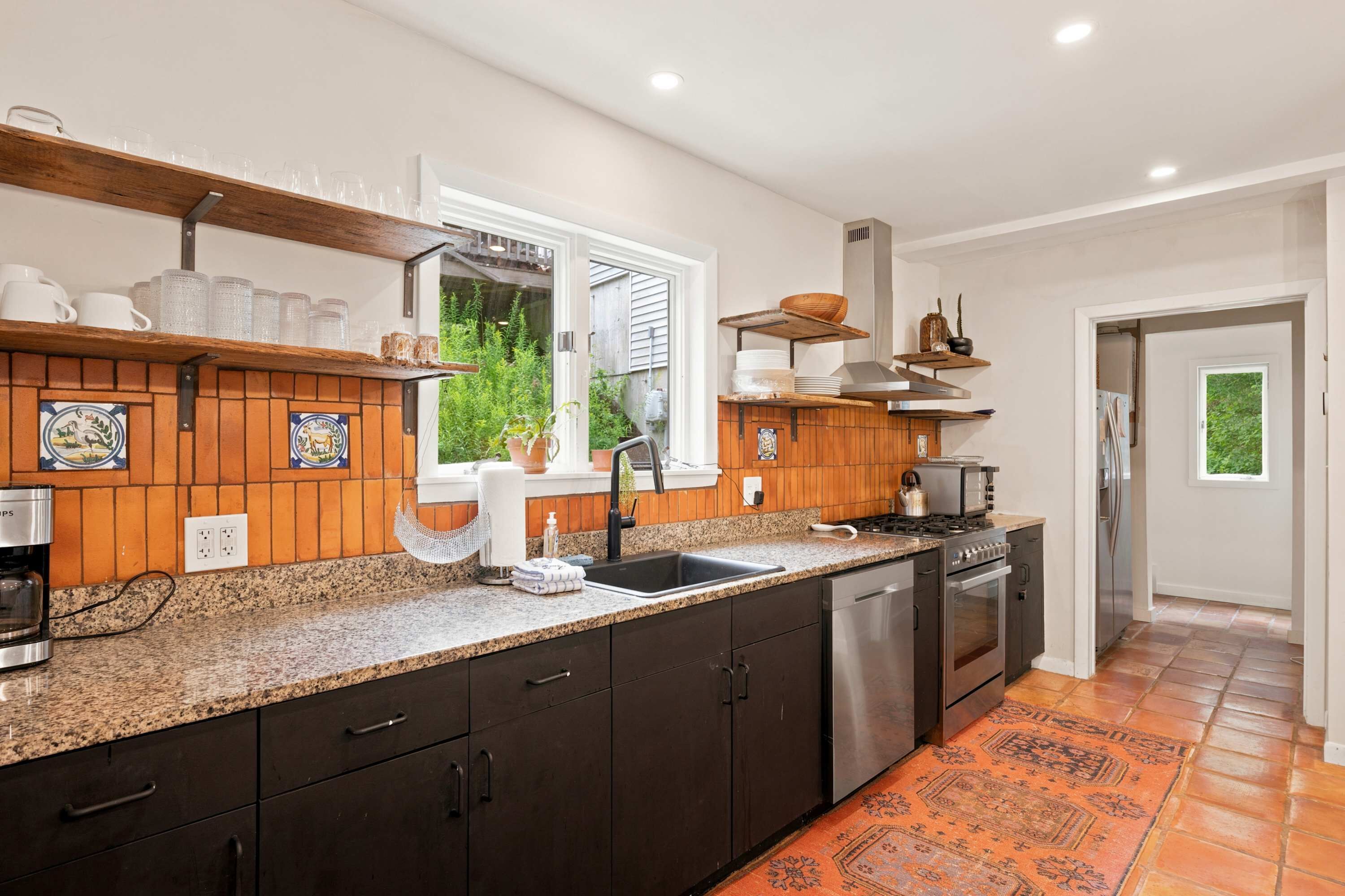 A modern kitchen with a granite countertop, dark cabinetry, and stainless steel appliances.