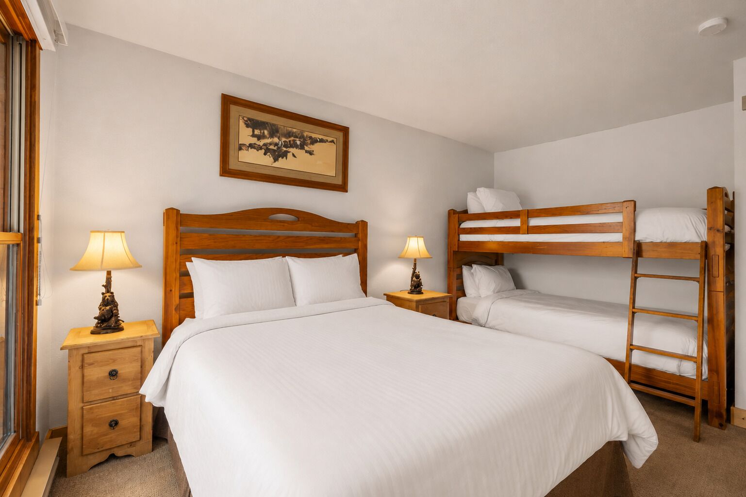 A bedroom with a large bed, two bedside tables with lamps, a bunk bed, and a framed picture on the wall.