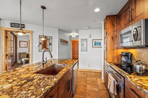 A kitchen with a granite countertop, stainless steel appliances, wooden cabinets, and a hanging light fixture. - Steps from Steamboat Resort Condo 1081 (Steamboat Springs)
