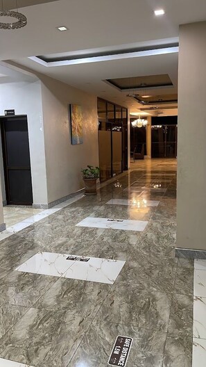 A hotel corridor with a marble floor, a potted plant, and a sign indicating a safe distance of 1.5 meters.