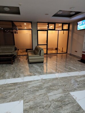 A hotel lobby with a marble floor, a sofa, a chair, and a television on the wall. - Grand Winston Hotel (Nakuru)