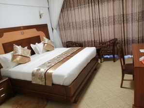 A hotel room with a bed, a wooden headboard, a desk, and a chair. - Grand Winston Hotel (Nakuru)