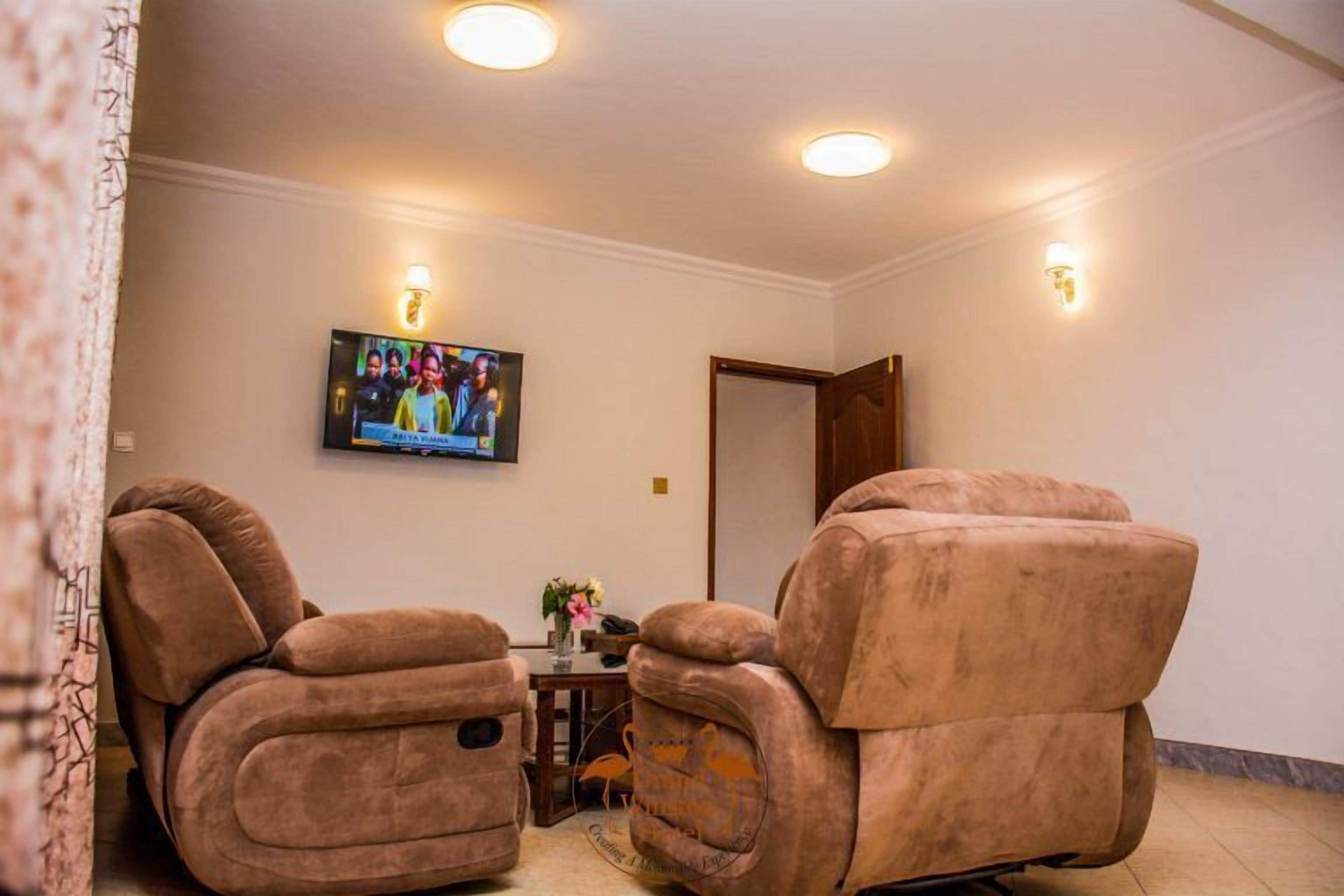 Um quarto com duas cadeiras de massagem, uma televisão na parede e uma pequena mesa com um vaso.