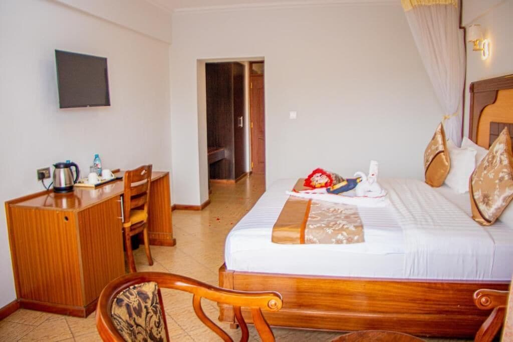 Una habitación de hotel con una cama, un escritorio, una silla y un televisor en la pared.