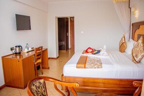 A hotel room with a bed, a desk, a chair, and a television on the wall.