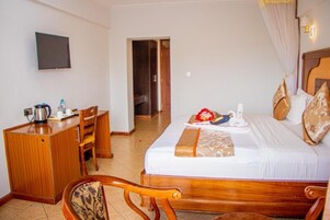 Una habitación de hotel con una cama, un escritorio, una silla y un televisor en la pared.