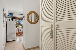 A hallway with a white door, a wicker mirror, and a view into a room with a table and chairs. - Casa Letizia: a cheerful apartment 200 meters from the sea with a veranda overlooking the bay (Nodu Pianu)