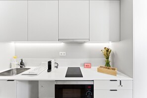 A modern kitchen with white cabinetry, a built-in oven, a coffee machine, and a small plant on the counter. - GuestReady - Studio near Porto Universities (São Mamede de Infesta)
