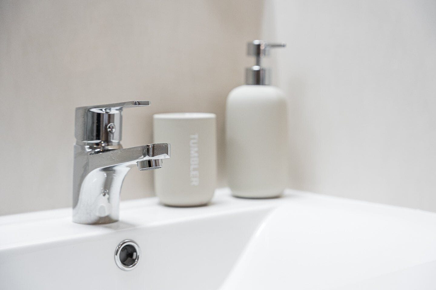 A modern bathroom sink with a chrome faucet, a white soap dispenser, and a bottle of liquid soap.