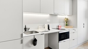 Moderni keittiö, jossa on valkoiset kaapit, ruostumattomasta teräksestä valmistettu allas, sisäänrakennettu uuni ja työtaso, jonka päällä on maljakko täynnä kukkia.