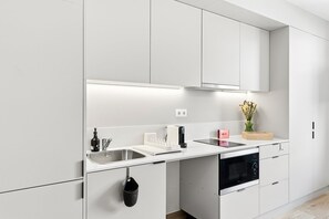 A modern kitchen with white cabinetry, a stainless steel sink, a built-in oven, and a countertop with a vase of flowers. - GuestReady - Studio near Porto Universities (São Mamede de Infesta)