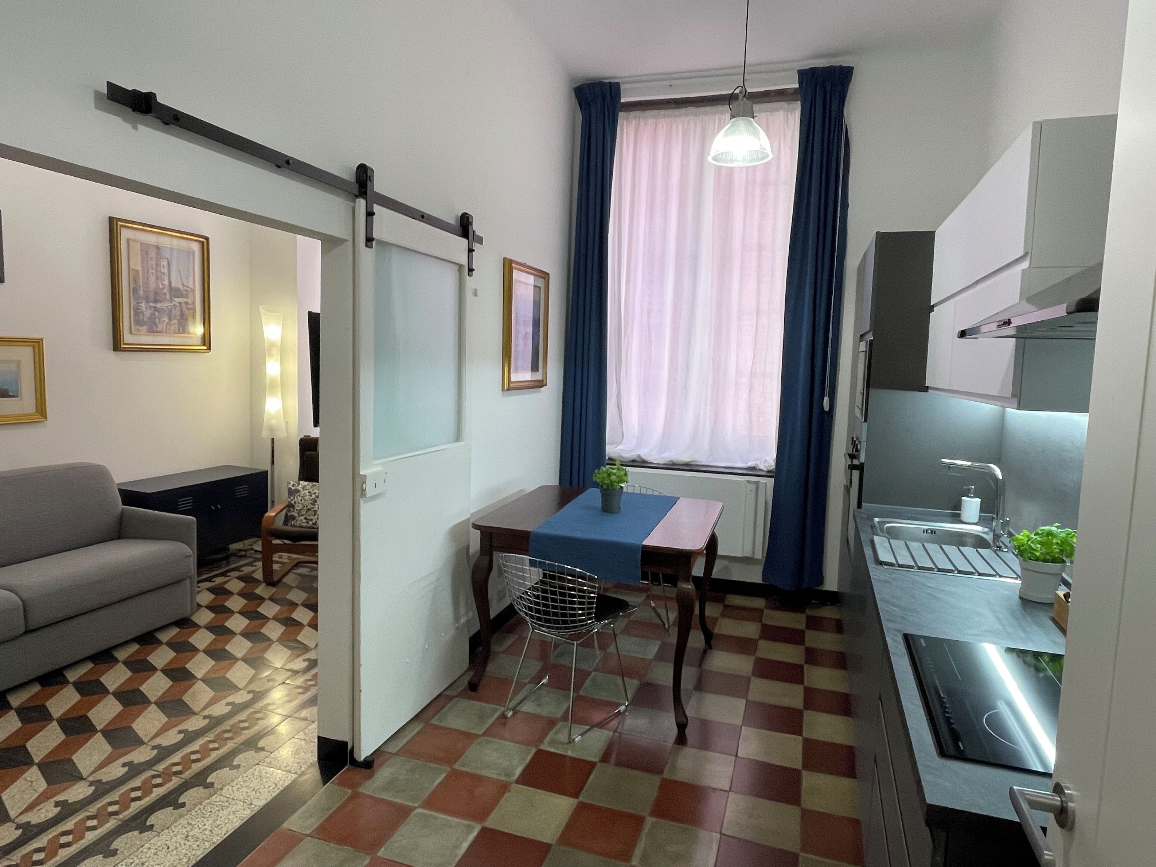 Un ambiente compatto con divano, tavolo da pranzo con sedie, angolo cottura e finestra con tende.