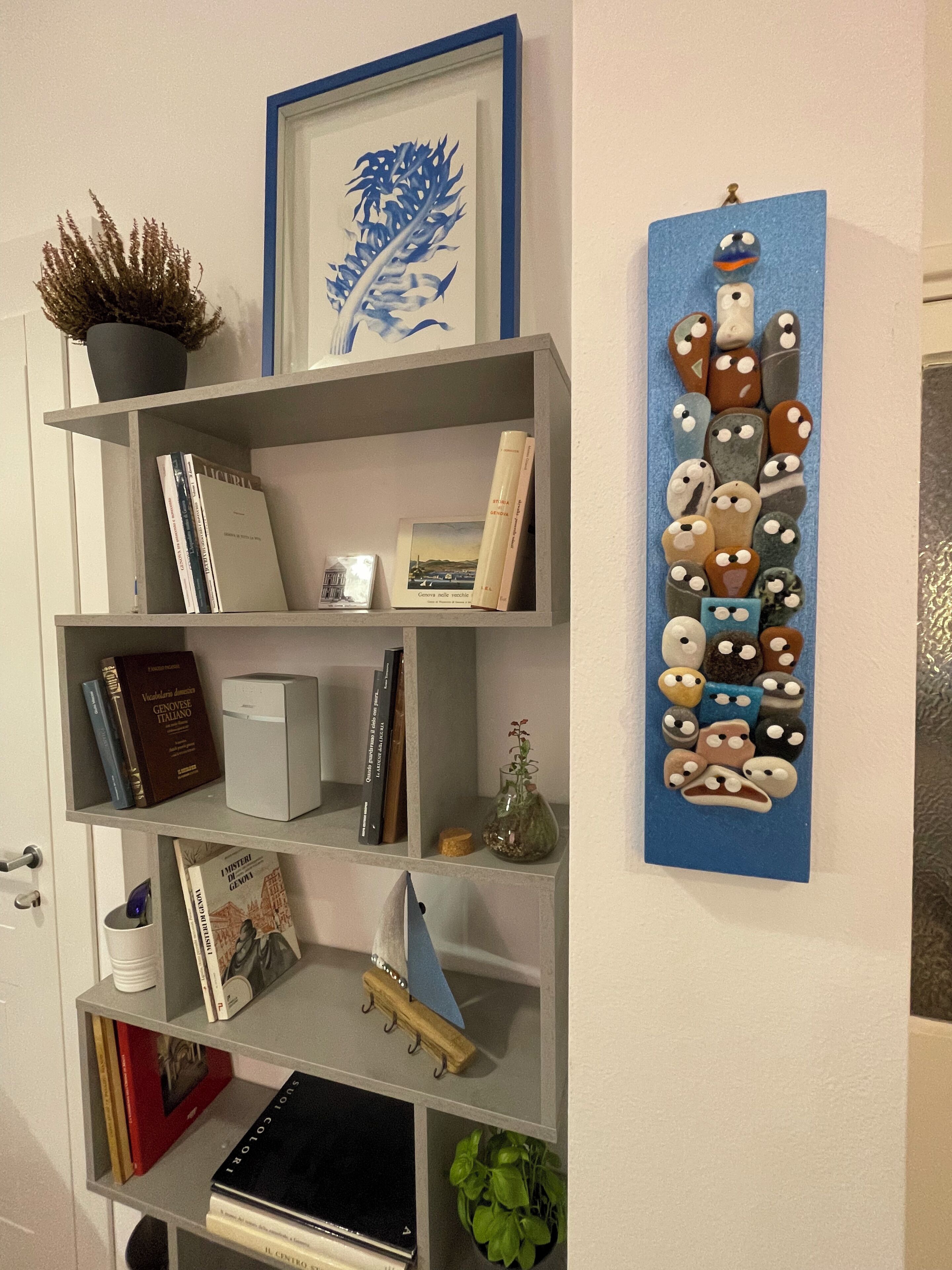 Una libreria con libri, un quadro incorniciato e un elemento decorativo a parete.