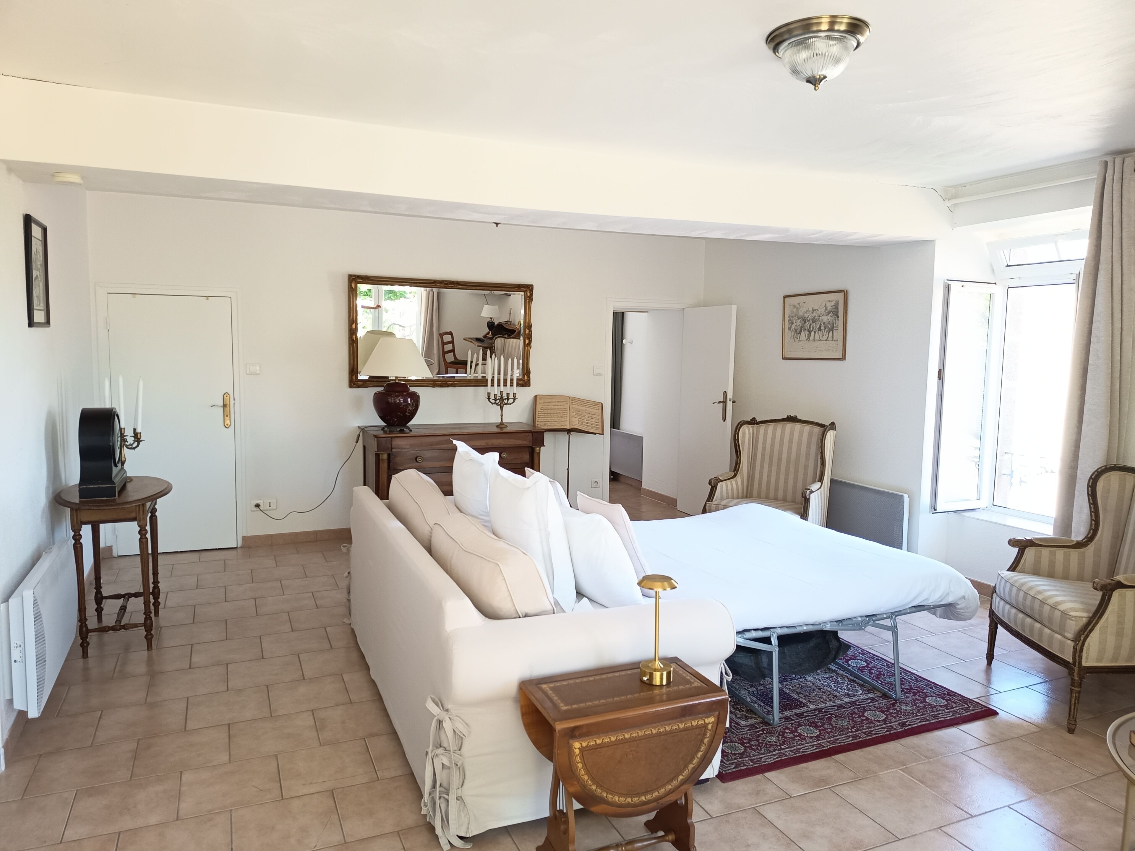 Une chambre d’hôtel avec un lit, un canapé, une chaise, une petite table, un miroir et une fenêtre.