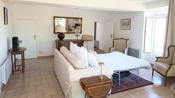 Ein Hotelzimmer mit einem Bett, einem Schlafsofa, einem Sessel, einem kleinen Tisch, einem Spiegel und einem Fenster.