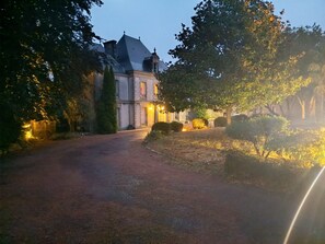 A building with a paved driveway leading to a gated entrance, surrounded by trees and shrubs. - La Pierre Levée Castle Lodging, 15 Min from Puy du Fou (La Gaubretière)