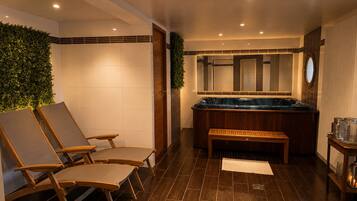Een wellnessruimte met een jacuzzi, houten lounge fauteuils en een klein tafeltje.