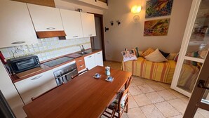A compact kitchen with a dining table, a toaster, and a sink. There is a sofa with cushions and a painting on the wall. - Callistemo Apartment (Rio)
